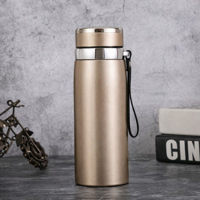 Gold insulated bottle with a black strap on a gray surface with a textured background