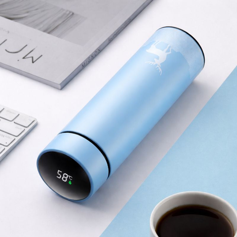Blue smart thermos with digital display on a desk with a cup of coffee and laptop.