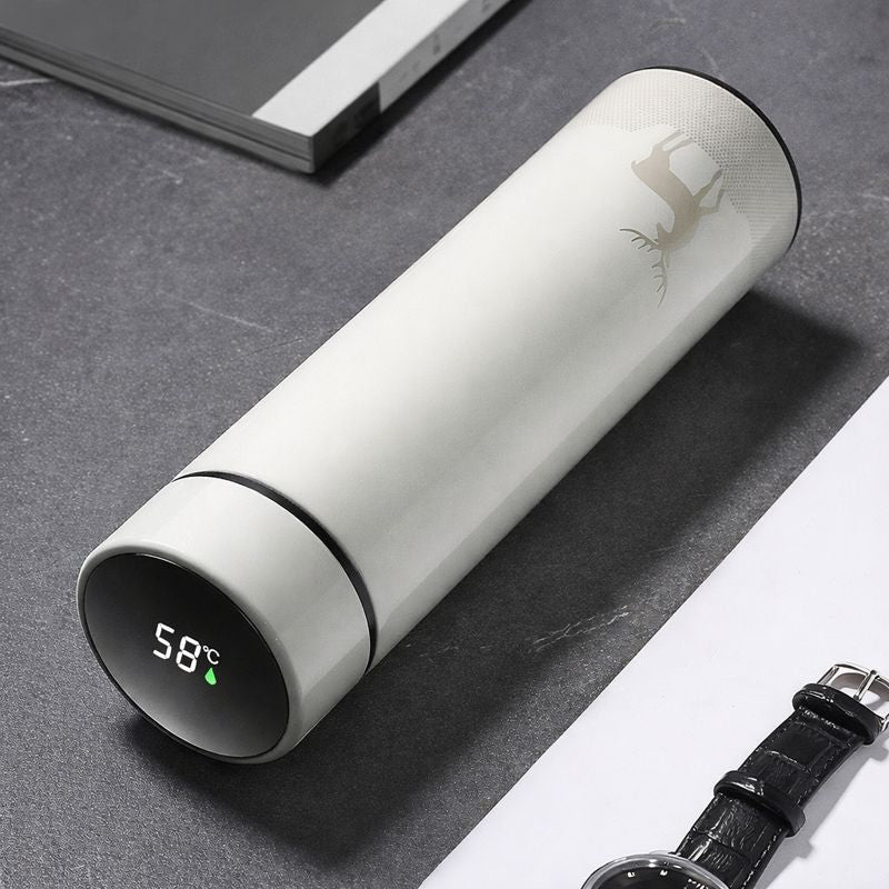White thermos bottle with digital temperature display on a gray surface with a watch.