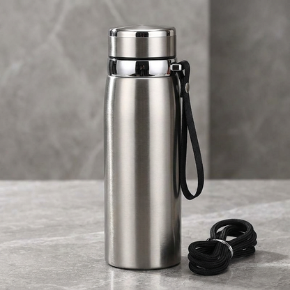 Stainless steel water bottle with black strap on a gray surface