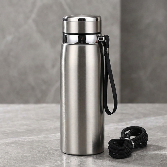 Stainless steel water bottle with black strap on a gray surface