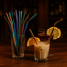 Colorful straws in a glass with a cocktail and lemon slice on a wooden surface.