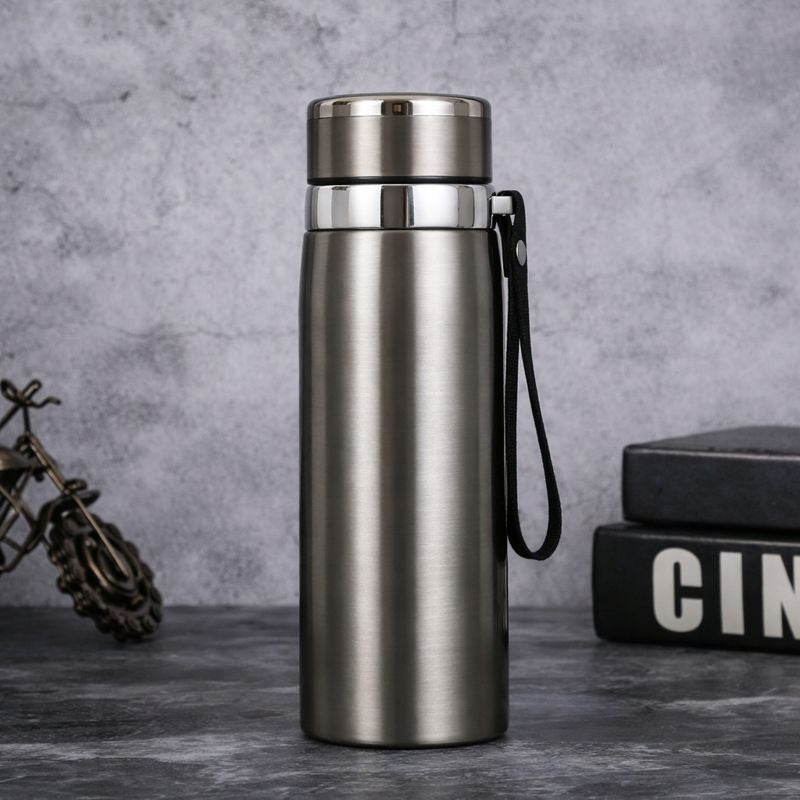 Silver insulated bottle with a black handle on a gray surface with a textured background.