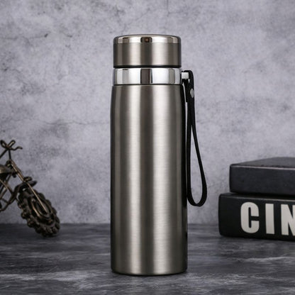 Silver insulated bottle with a black handle on a gray surface with a textured background.